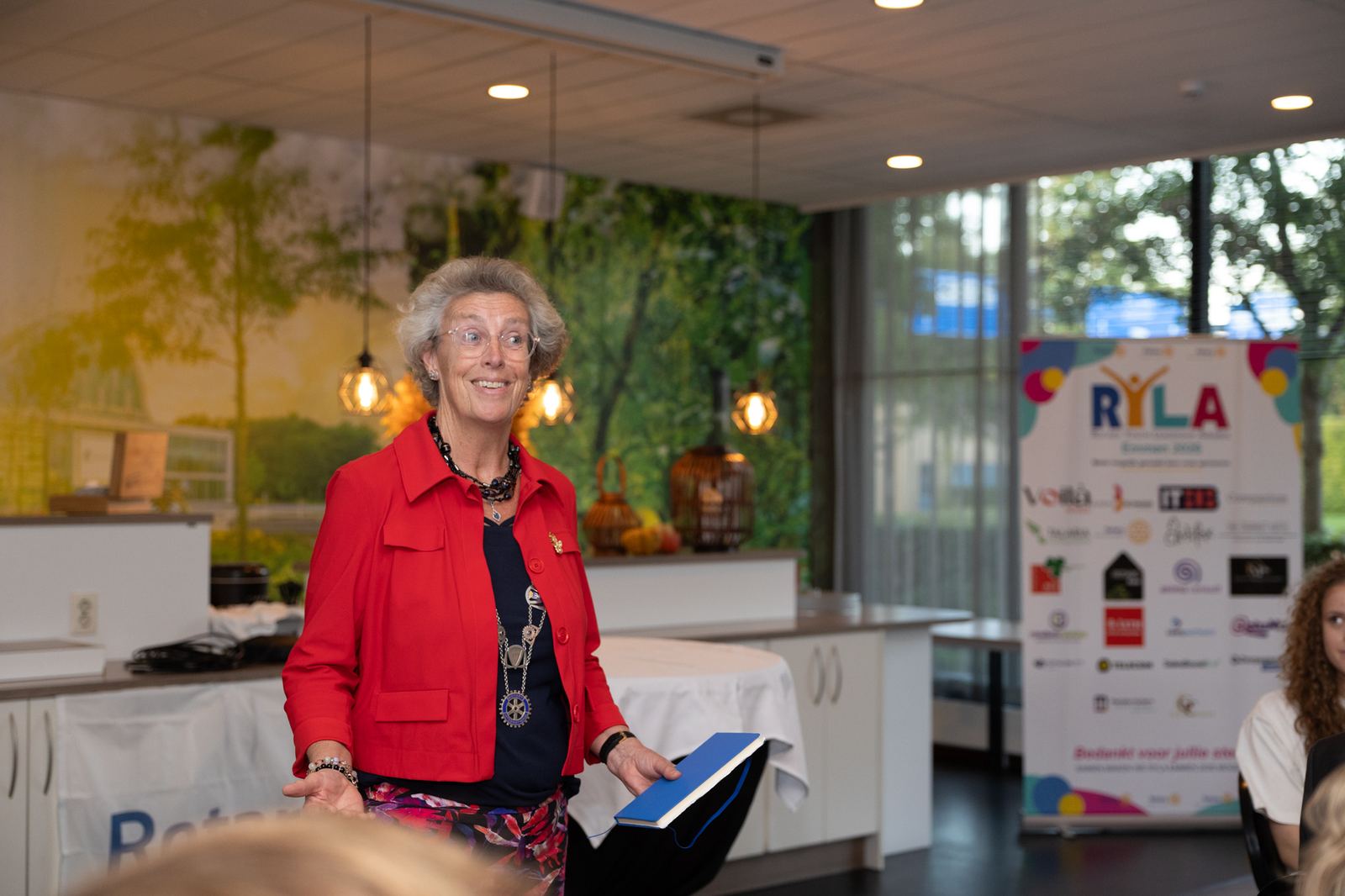 Gouverneur Marian Strating staat in een rode jas en heet de deelnemers welkom